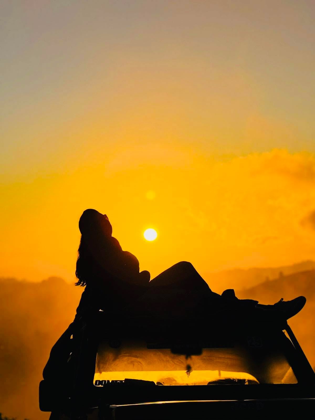 Silhouette of a traveller on a jeep roof at Mount Batur sunrise