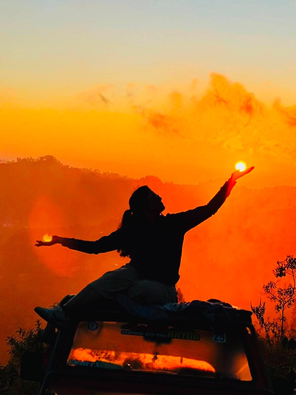 Traveller silhouetted on a jeep roof holding the sun at Mount Batur